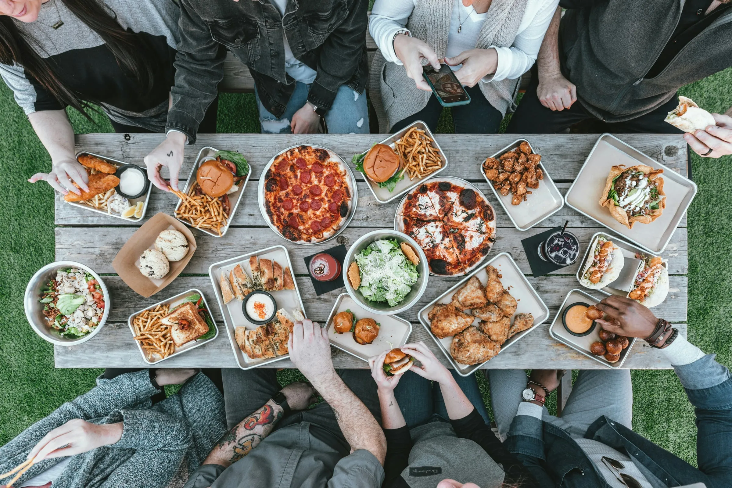 Overhead view of friends gathered around a wooden table covered with shared food